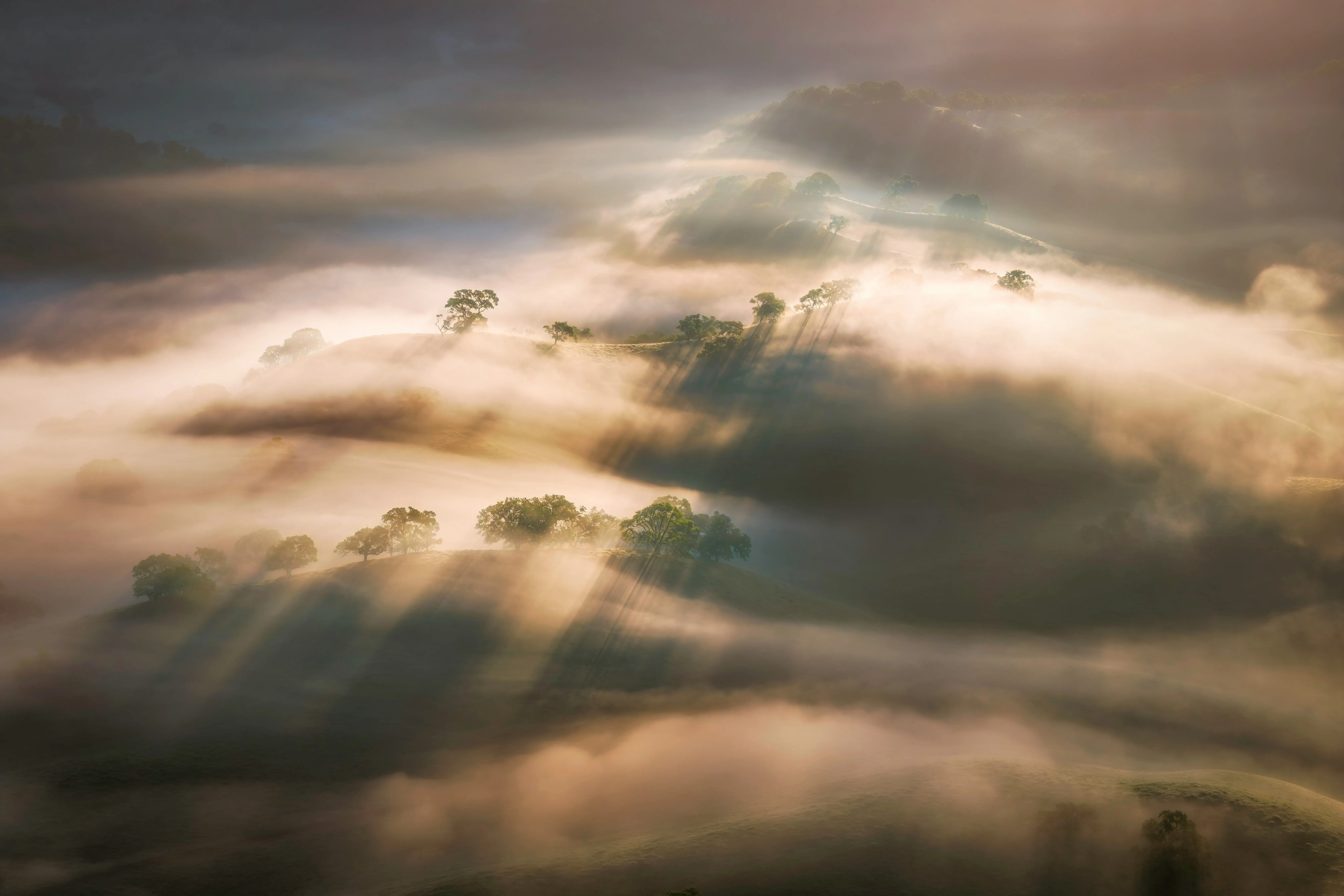Sun rays visible through clouds over rolling hills