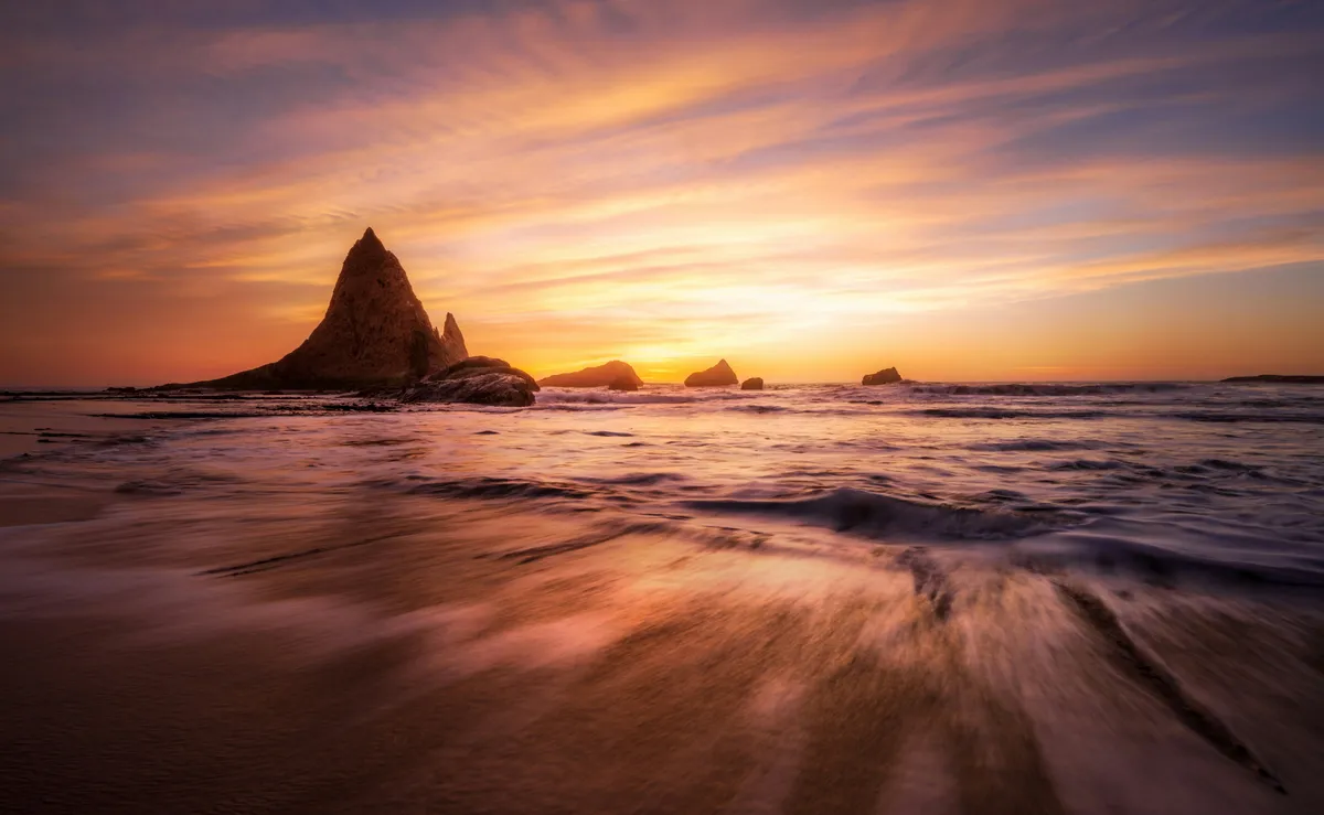 Rocks jutting out against the sky from the shore in a sunset beach photo